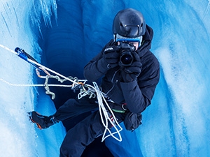 A man hangs over an icy hole pointing his camera above